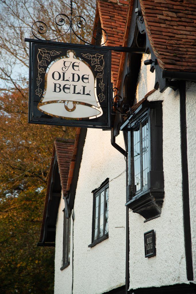 Vintage pub sign reading 'Ye Olde Bell' hangs from traditional Tudor-style building.