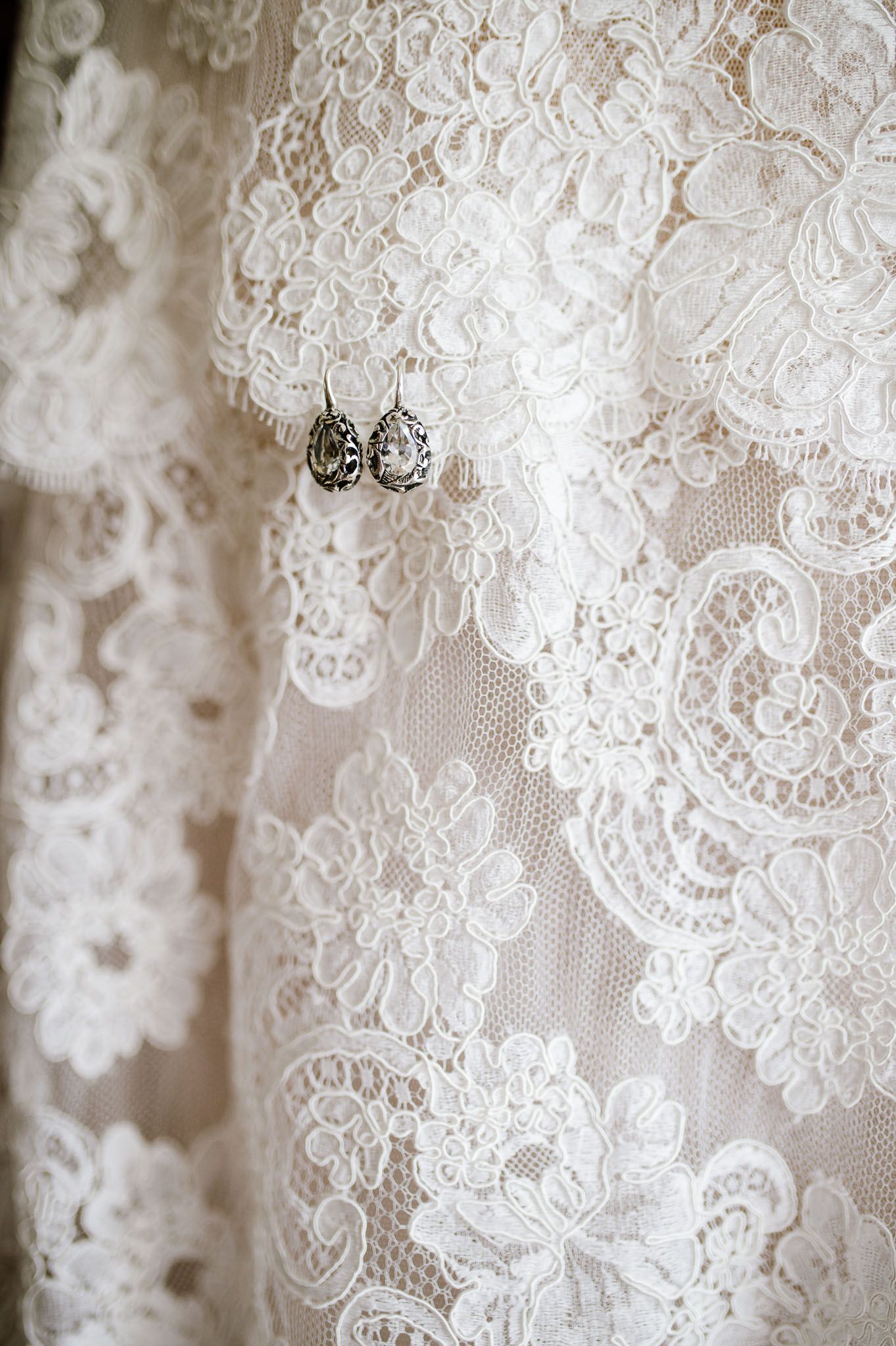 Delicate white lace wedding dress detail with vintage-style earrings.