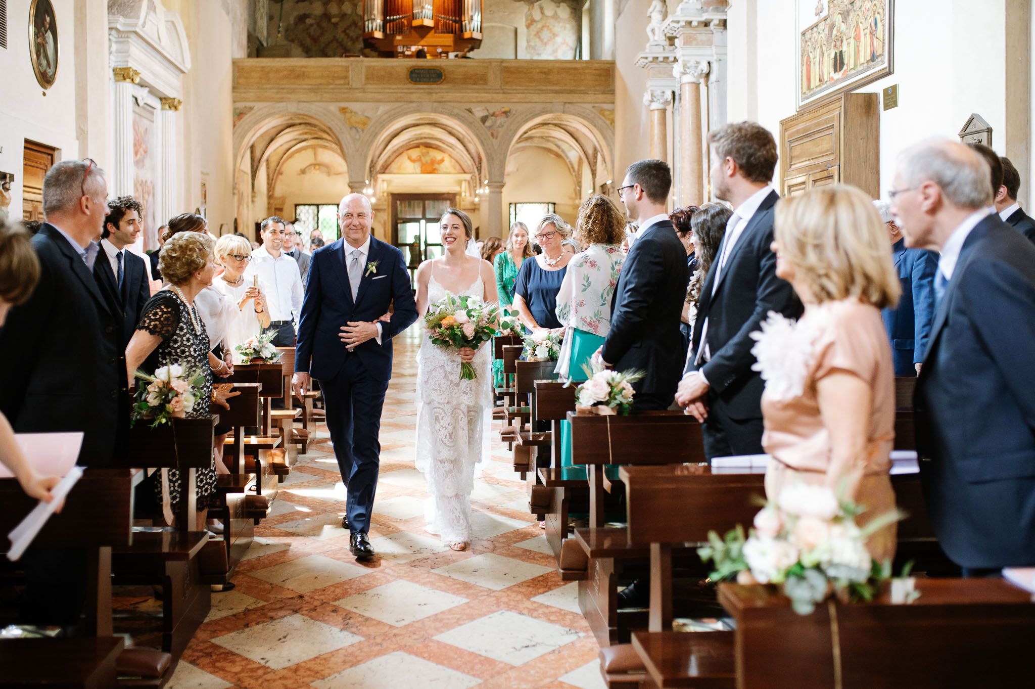 Wedding ceremony in progress inside historic church with guests standing in decorated aisle.