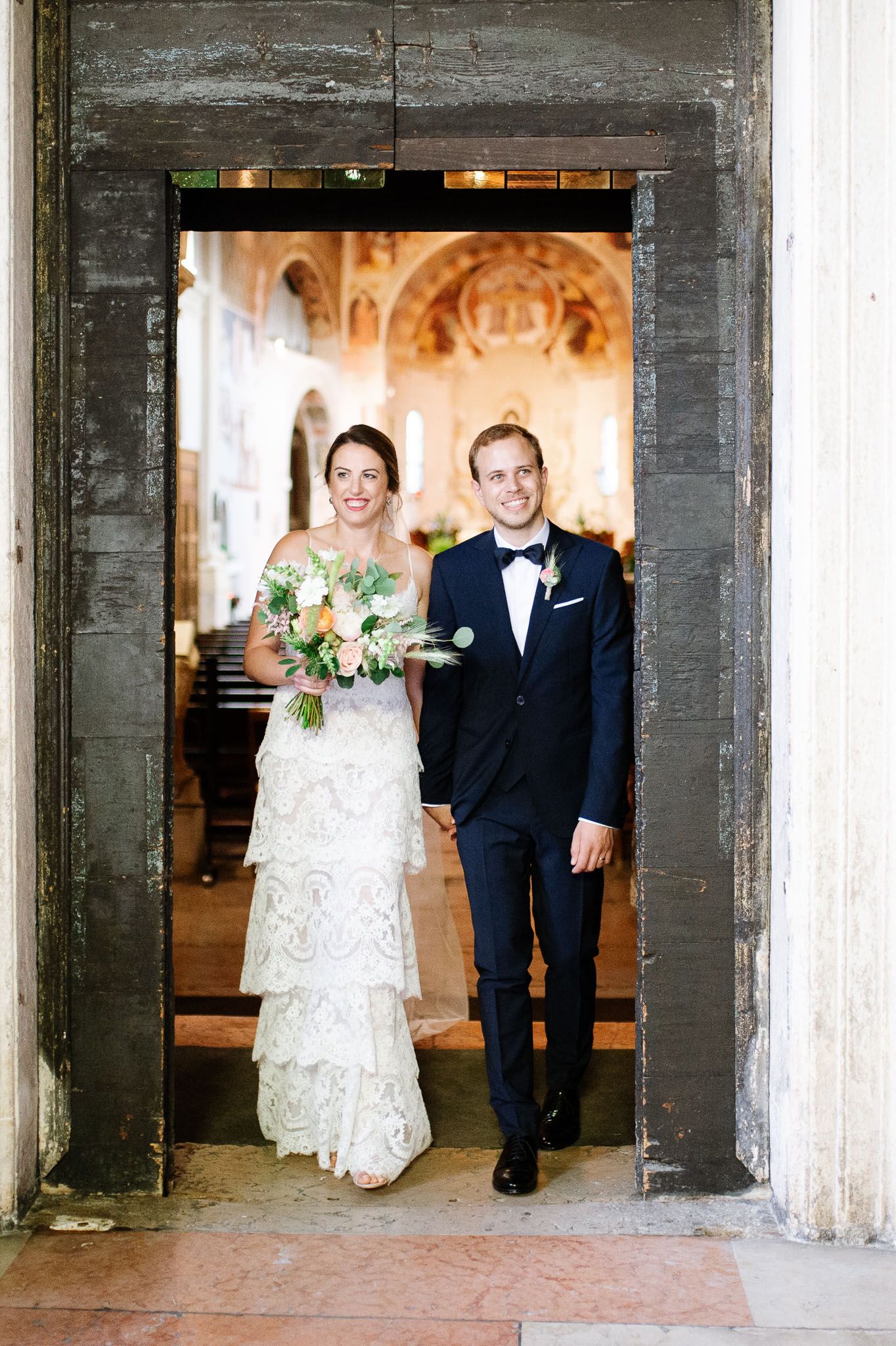 Newlywed couple exiting church through rustic doorway after wedding ceremony.