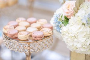 Pink macarons displayed on a crystal cake stand next to white hydrangeas.