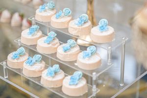 Delicate pink desserts topped with light blue decorations arranged on a clear tiered display.