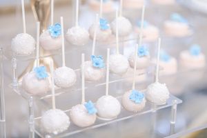 White cake pops decorated with blue accents displayed on a tiered acrylic stand.