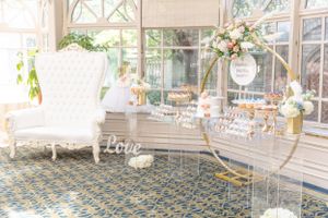 Luxurious bridal shower setup with vintage white chair and floral arrangements in a sunlit room.