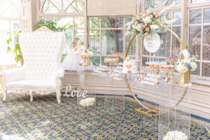 Bright sunlit room with white throne chair and gold circular dessert display stands.