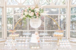 Wedding dessert display with gold circular arch and pink floral arrangements.