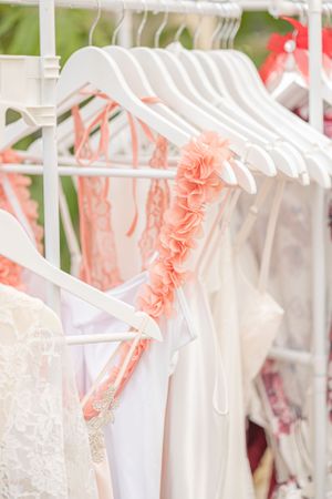 White hangers with delicate coral pink floral embellishments displayed on a clothing rack.