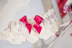 White lace wedding garter adorned with a pink bow and crystal embellishment.