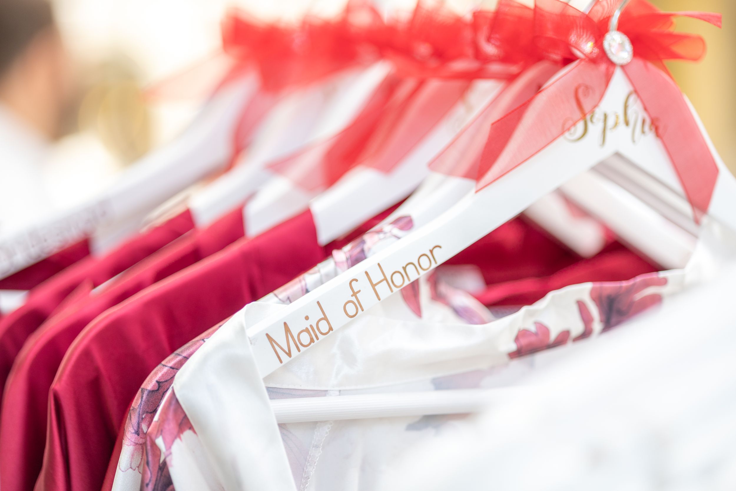 Red and white bridesmaids robes hanging neatly on white hangers in a row.