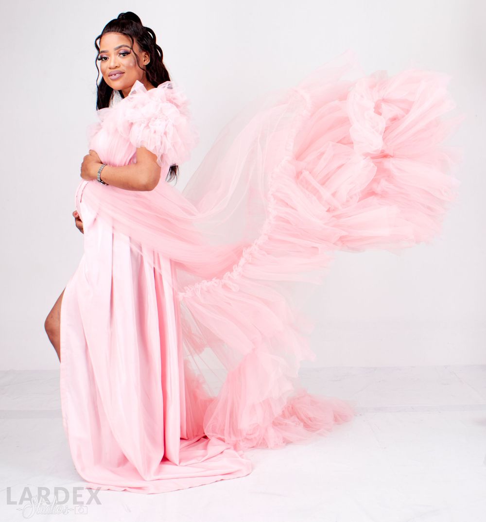 Ethereal maternity portrait with flowing pink tulle fabric creating dramatic movement.