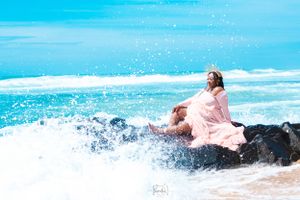 Dreamy beach maternity photo with waves splashing against rocks.