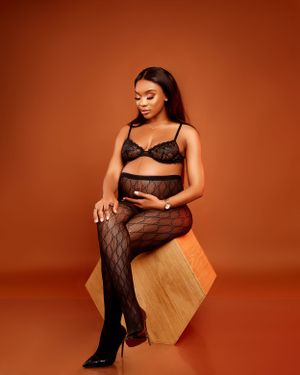 Maternity boudoir photo with figure seated on geometric prop against warm brown background.
