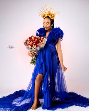 Maternity portrait in blue gown with golden crown holding red flower bouquet.