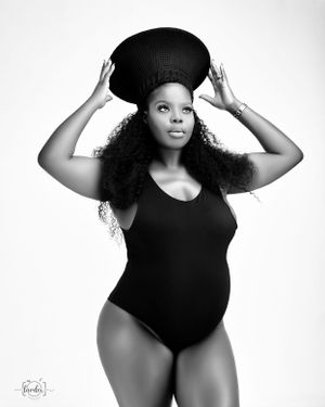Black and white maternity portrait with spherical prop balanced on head.