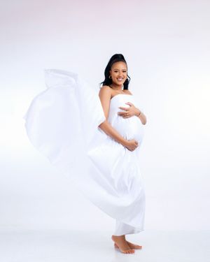 Dynamic maternity portrait with flowing white fabric against light background.