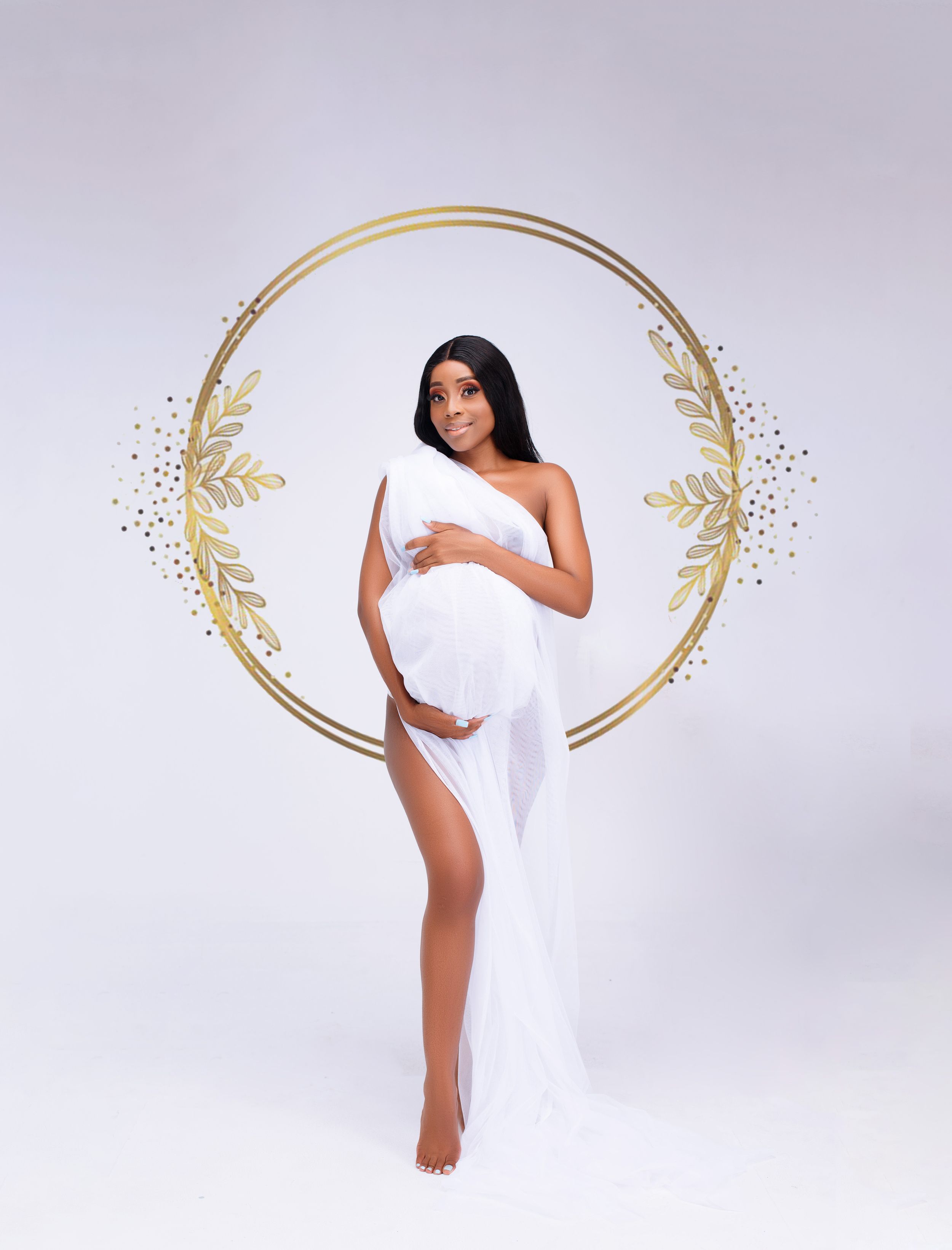 Ethereal maternity portrait with white fabric and golden circular frame decoration.