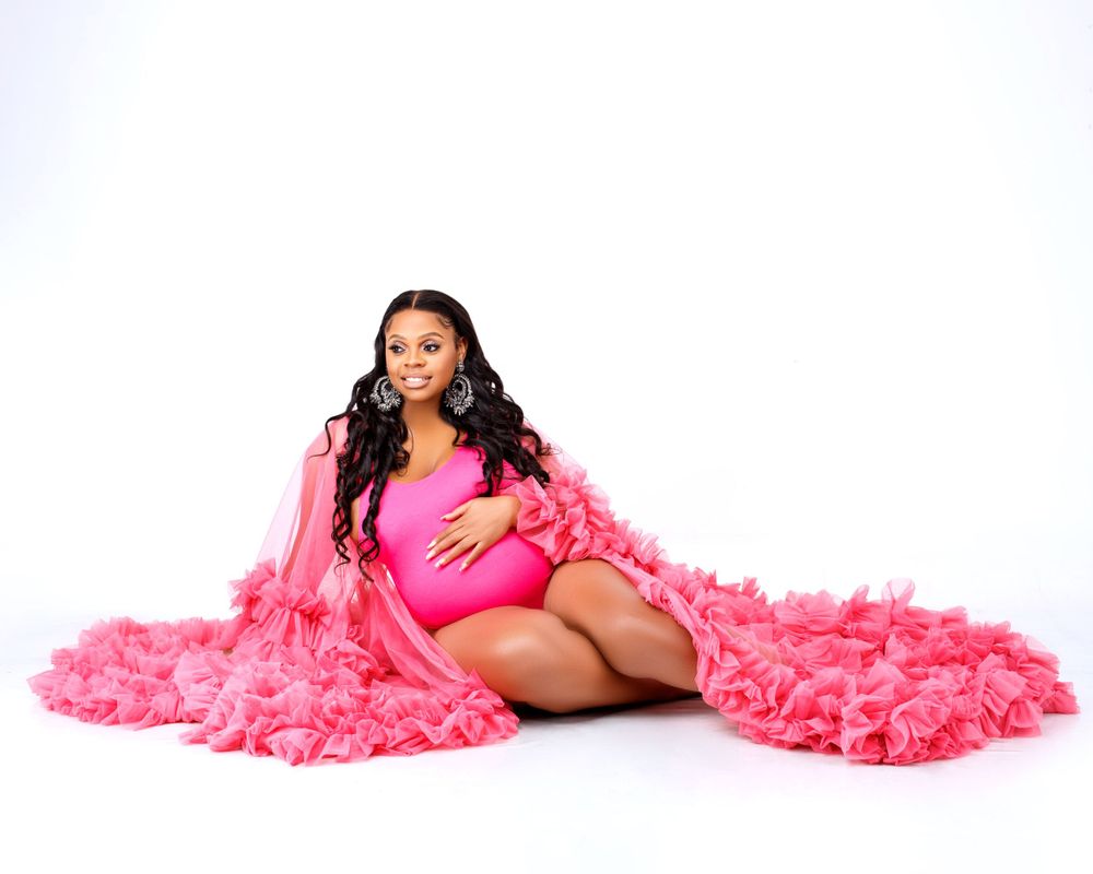 Maternity portrait with flowing pink tulle robe on white background.