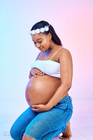 Sweet casual maternity portrait with white flower crown and denim against pastel background.