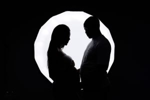 Romantic silhouette of expectant couple against glowing circular light background.