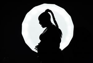 Dramatic silhouette of pregnant woman against glowing circular light backdrop.