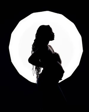 Dramatic silhouette of a pregnant figure against a bright circular light backdrop.