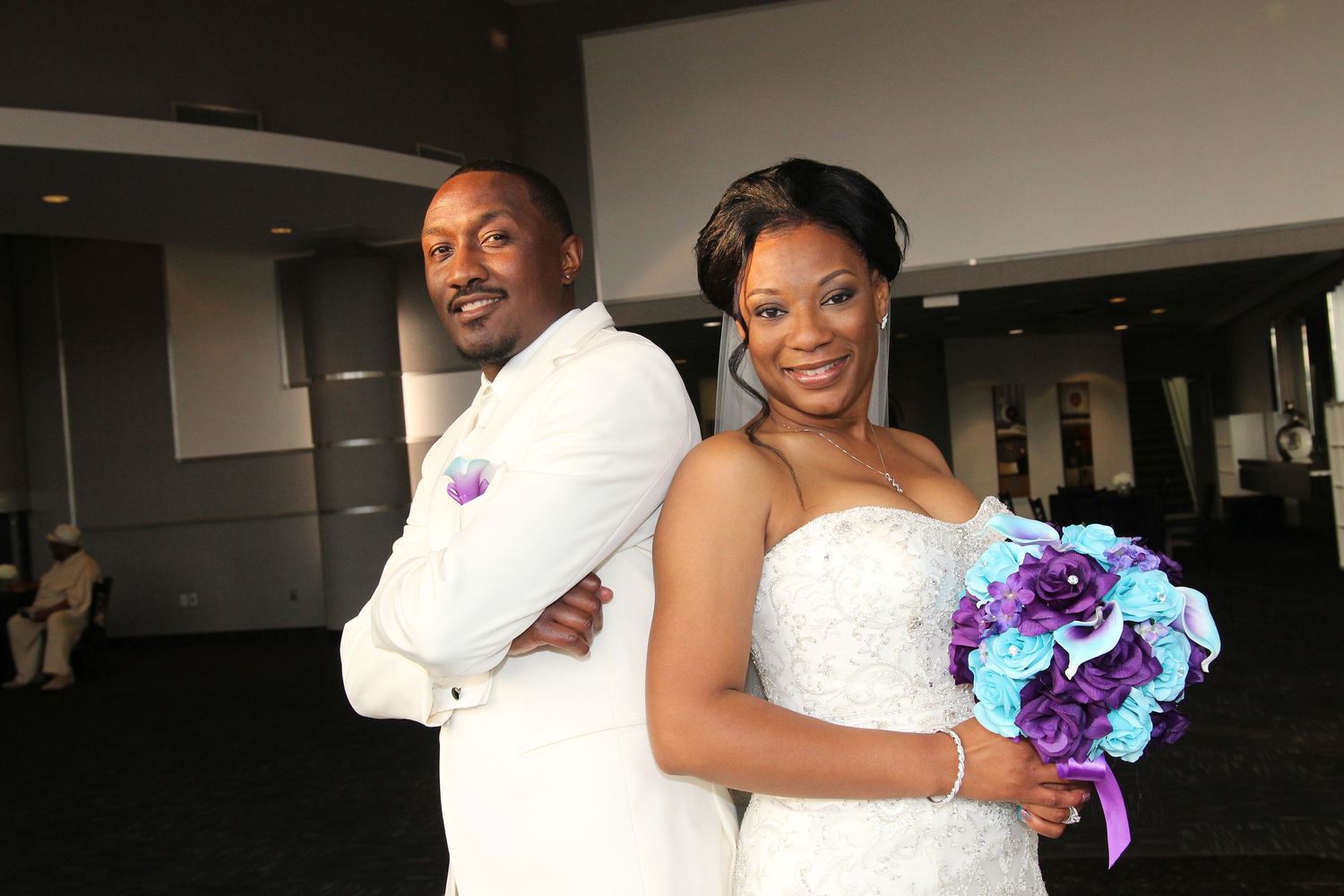 Wedding couple holding blue and purple bouquet in modern indoor setting.