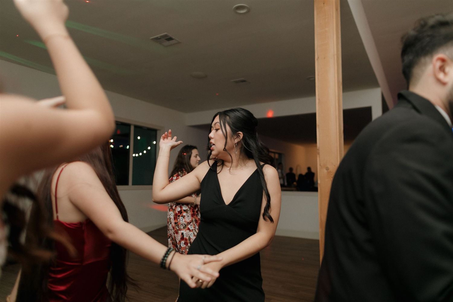 Party guests dancing together at an indoor reception with warm lighting and wooden beams.