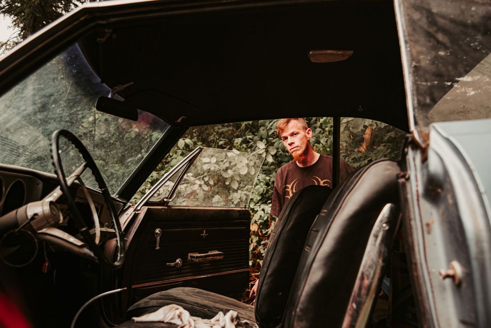 Young man looking into an old vintage car from the driver's side.