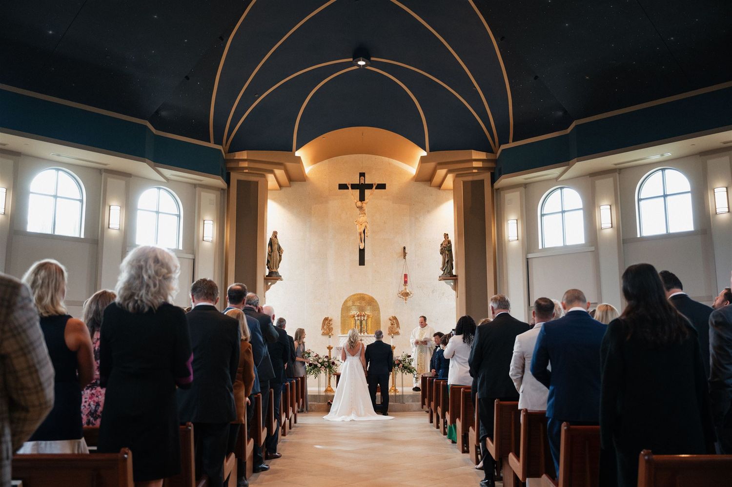 Wide view of traditional church wedding ceremony with vaulted ceiling and arched windows.
