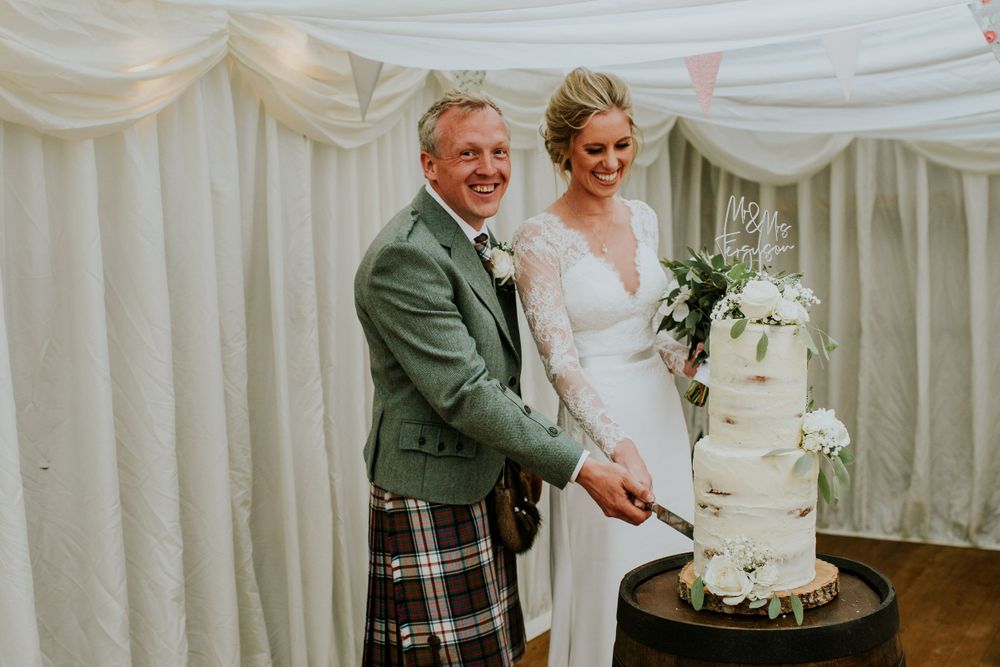 Wedding cake cutting moment in an elegant white draped reception venue.