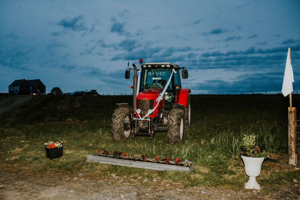 Red tractor parked against dramatic evening sky at outdoor wedding venue.