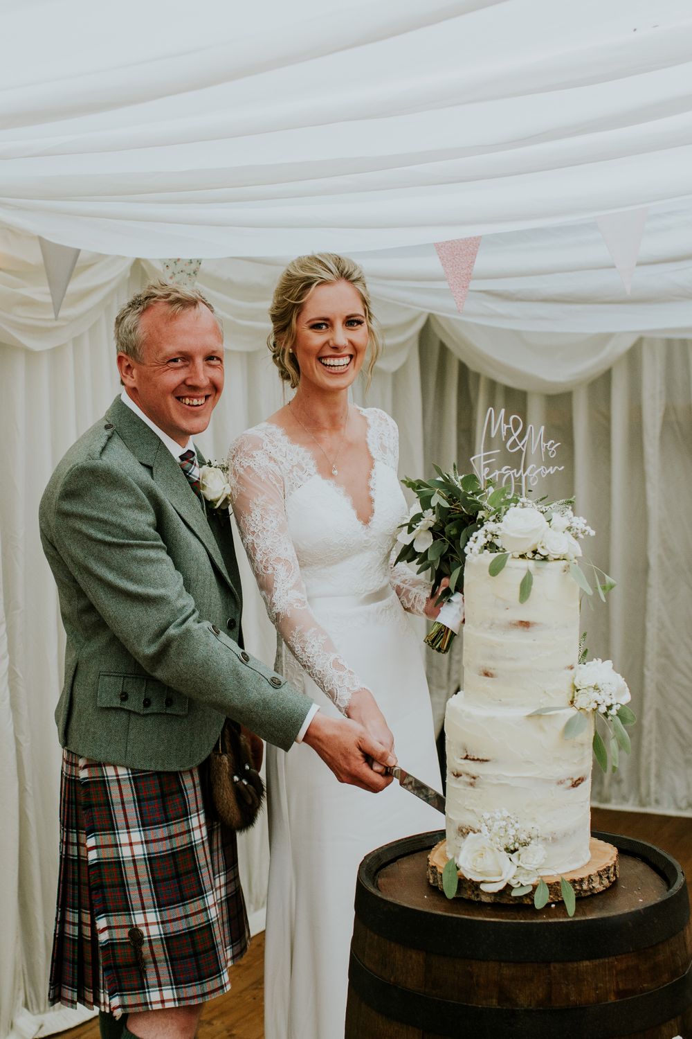 Joyful cake cutting moment at an elegant wedding reception with Scottish highland attire.