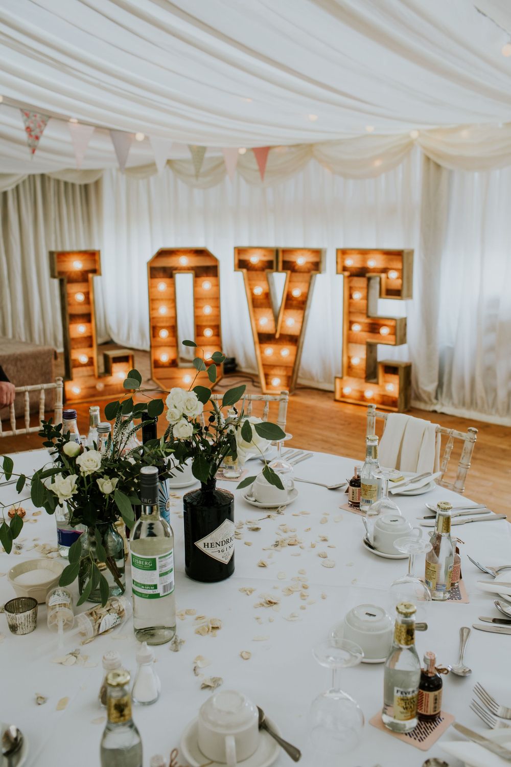 Illuminated LOVE marquee letters with floral arrangements and place settings at a wedding reception.