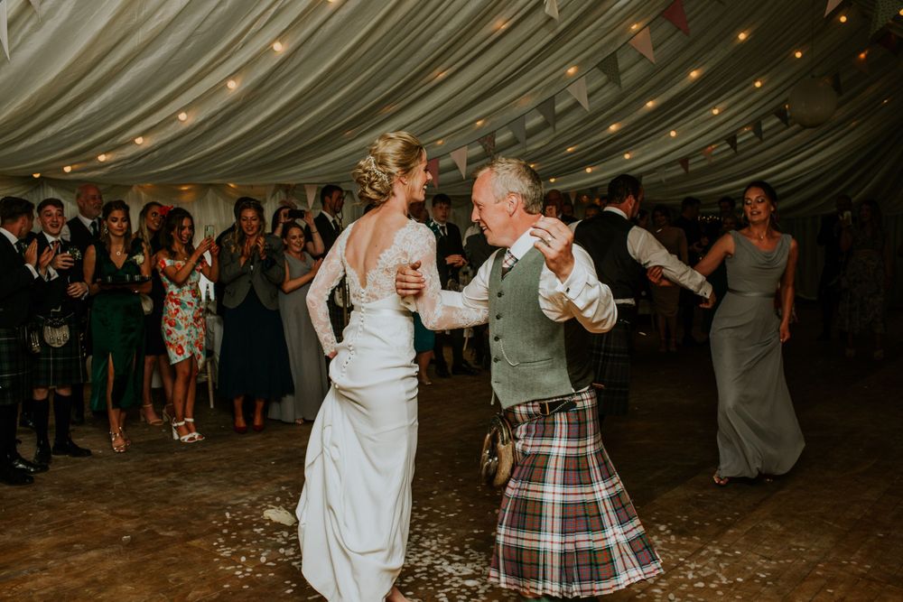 Dancing celebration at a wedding reception with traditional Scottish kilts under draped ceiling with twinkle lights.