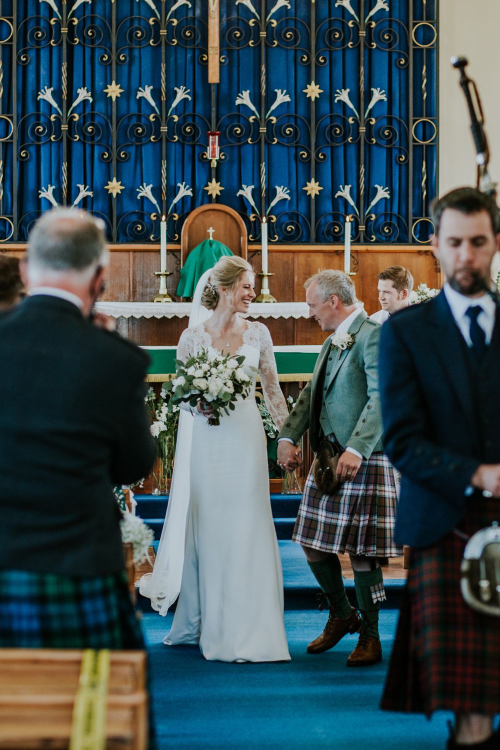 Church wedding ceremony with decorative blue altar screen and Scottish kilts.