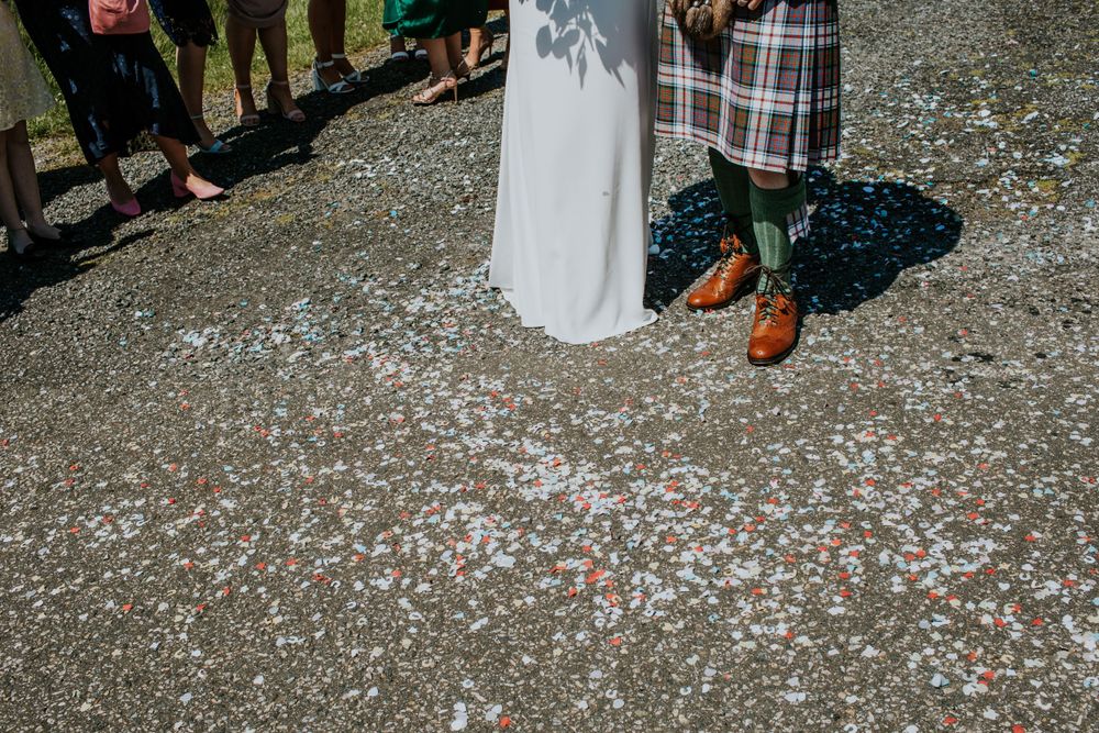 White wedding dress and traditional Scottish kilt with colorful confetti scattered on the ground.