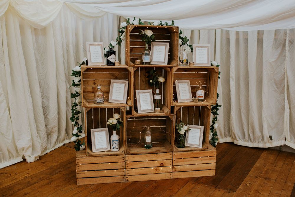 Rustic wooden crate display with decorative frames and floral accents against white draping.