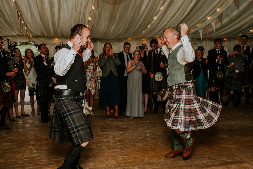 Traditional Scottish dancing performance at wedding reception under decorated tent.
