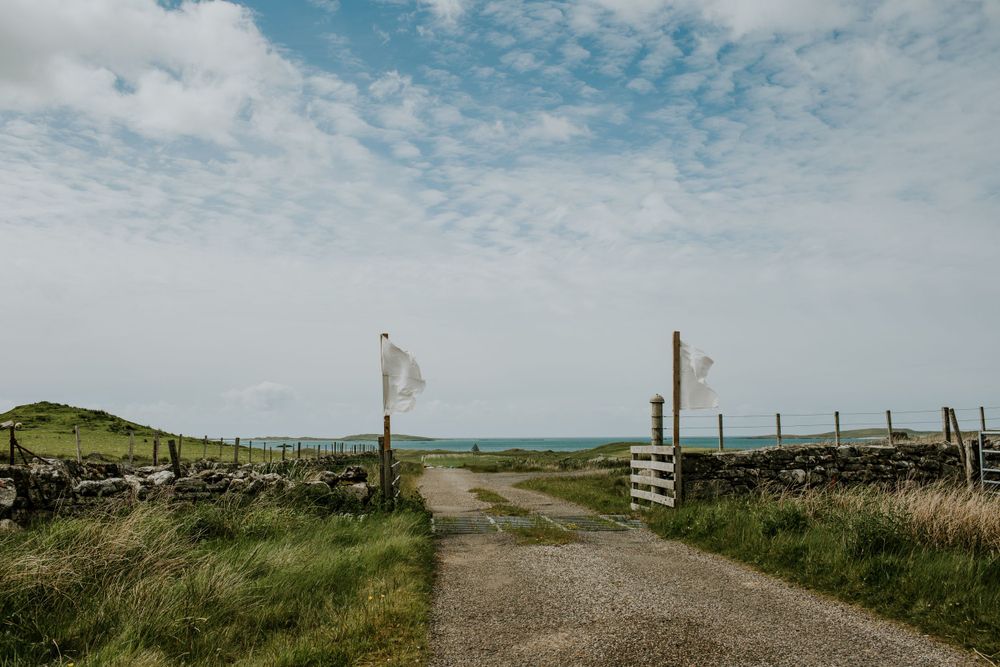Scenic countryside path with wooden gate leading to rolling green hills under cloudy skies.