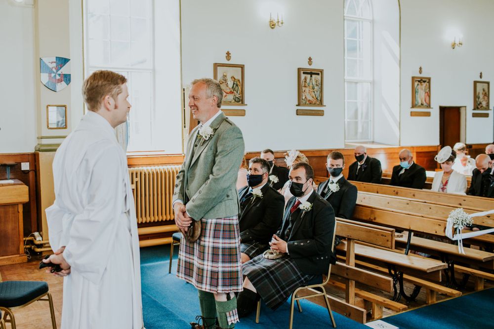 Church interior with traditional Scottish wedding attire and wooden pews.