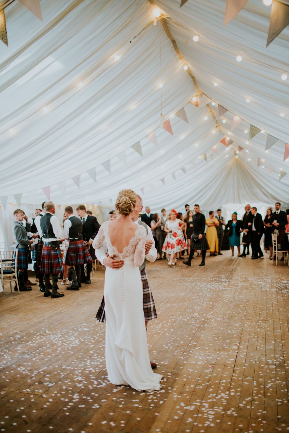 Elegant wedding reception in a white draped tent decorated with fairy lights and bunting.