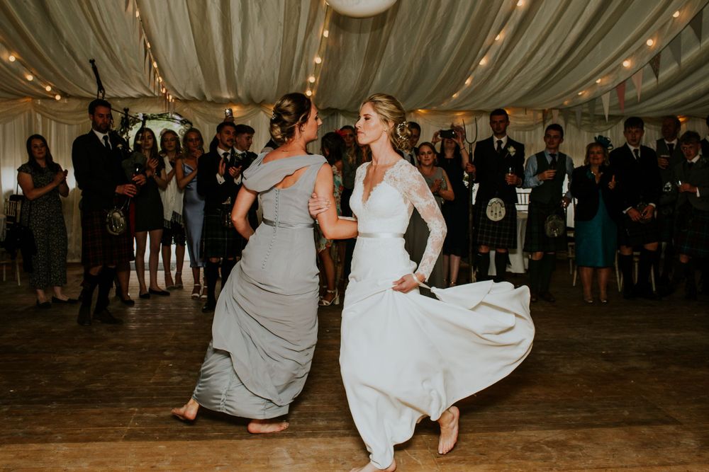 Dancing celebration at Scottish wedding reception under draped tent ceiling.