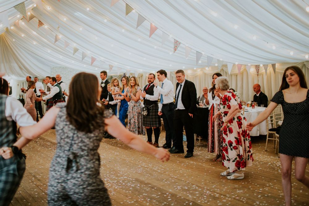 Guests dancing in a white marquee tent with decorative bunting during a wedding celebration.