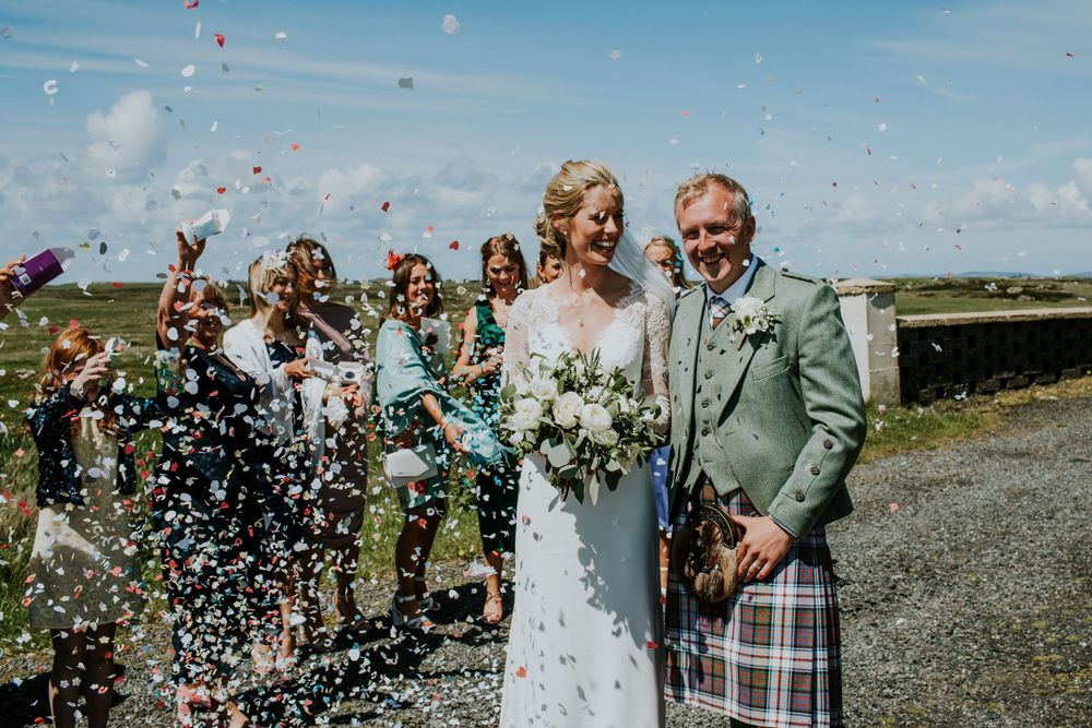 Wedding celebration outdoors with confetti being thrown under bright blue skies.