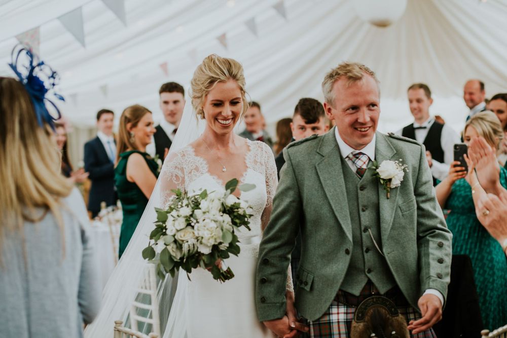 Wedding celebration in a white tent with traditional Scottish formal wear and festive decor.