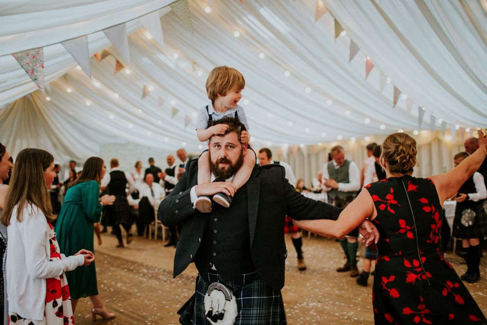 Traditional Scottish wedding celebration with kilted guests dancing in a decorated marquee.