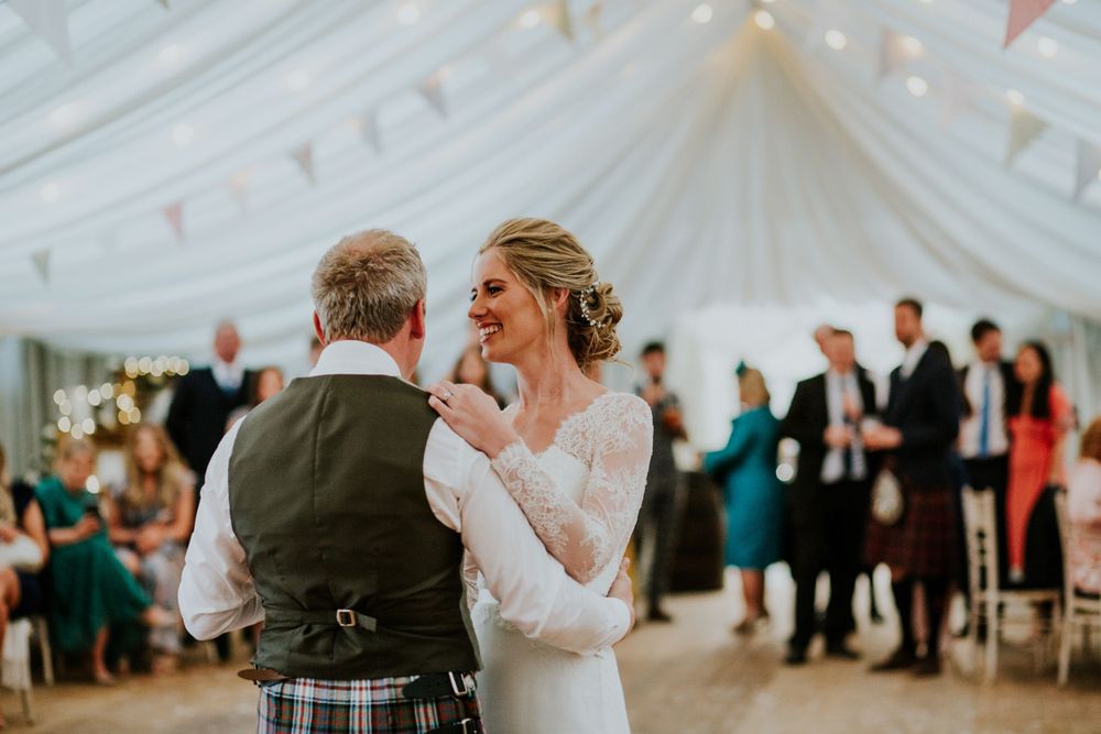 Intimate wedding dance moment in a white tent decorated with string lights and pastel bunting.