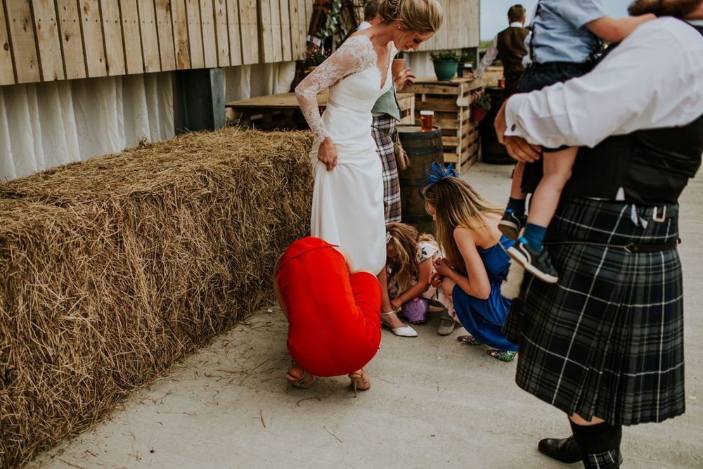 Wedding scene with hay bales and traditional Scottish kilts in rustic setting.