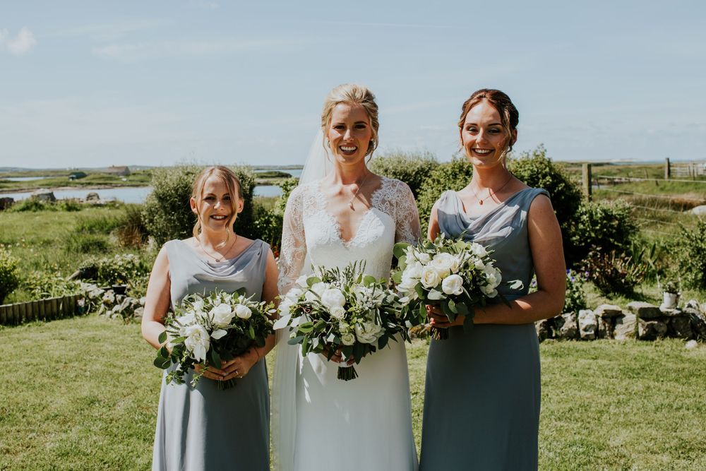 Wedding party poses with white bouquets against coastal landscape.