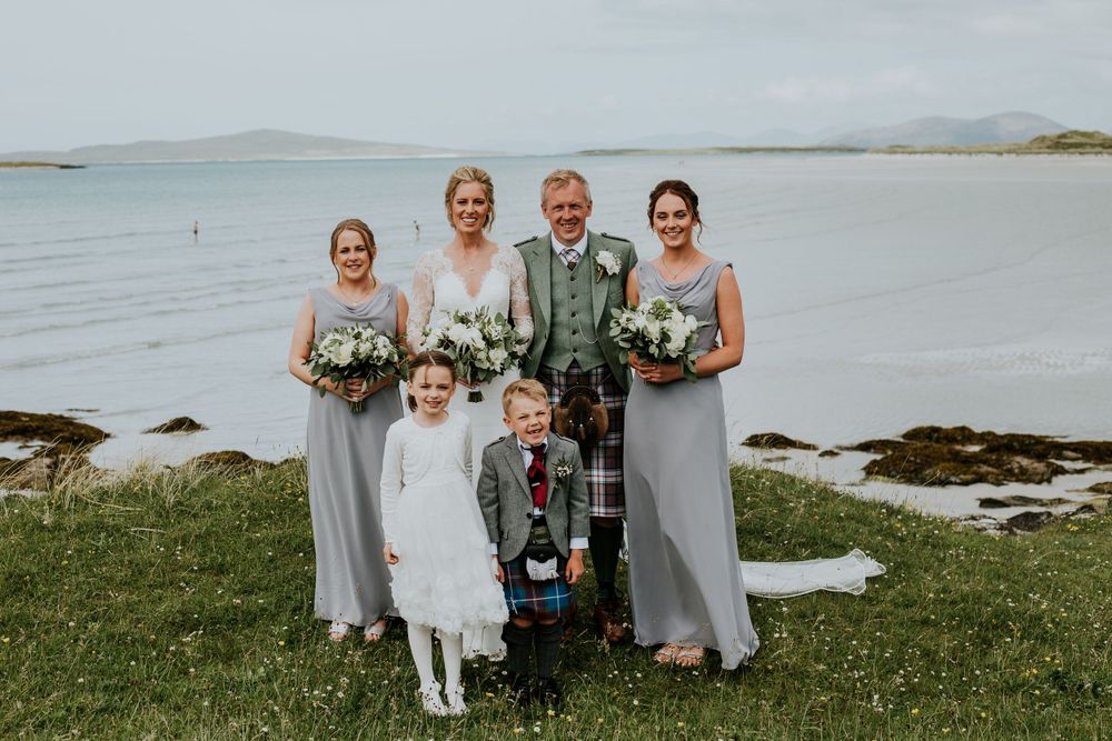 Wedding party in traditional Scottish attire posing by the seaside.